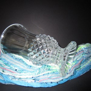 May include: A clear glass vase with a diamond-shaped pattern sits on a blue and green striped fabric.