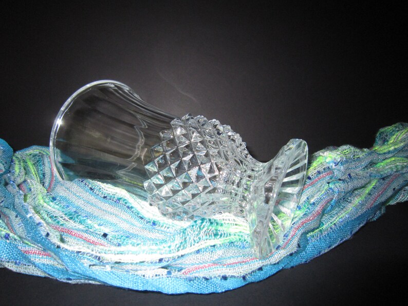 May include: A clear glass vase with a diamond-shaped pattern sits on a blue and green striped fabric.