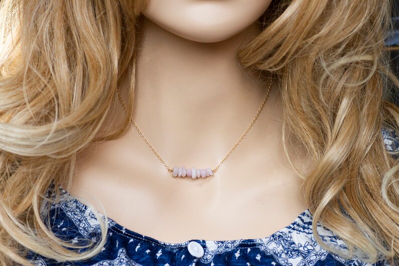 May include: A delicate gold chain necklace with a bar of light pink stones.