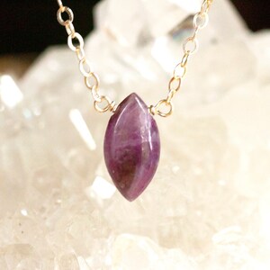 May include: A delicate gold chain necklace with a purple amethyst pendant. The pendant is a marquise shape and has a natural, raw look.