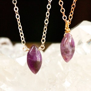 May include: Two gold necklaces with purple gemstone pendants. The pendants are shaped like teardrops and are set in gold wire.