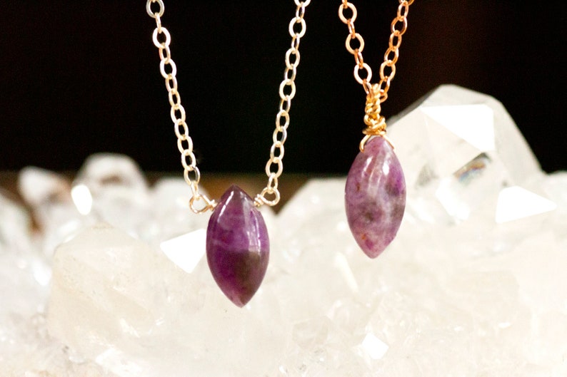 May include: Two gold necklaces with purple gemstone pendants. The pendants are shaped like teardrops and are set in gold wire.