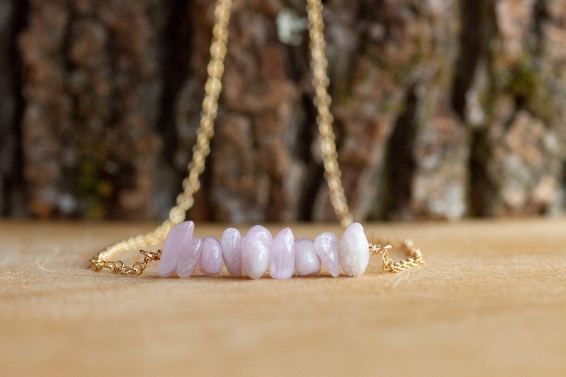May include: A delicate gold chain necklace with a bar of light pink and white stones.