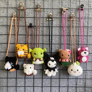 May include: A collection of handmade crochet character pouches, each with a cord for wearing. The pouches feature various designs, including a black cat, tiger, Shrek, My Melody, Hello Kitty, bear, and an onion.