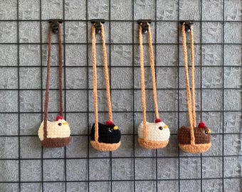 Könnte beinhalten: Vier gehäkelte, hühnerförmige Ornamente hängen vor einem Gitterhintergrund. Jedes Ornament hat ein anderes Farbschema: Braun und Creme, Schwarz, Creme und Beige sowie Braun. Sie haben rote Kammdetails und gelbe Schnäbel.