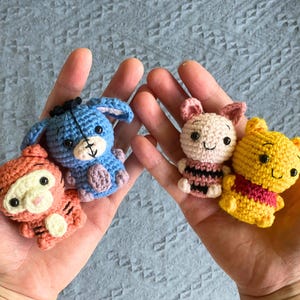 Può includere: Giocattoli all'uncinetto dei personaggi di Winnie the Pooh: Tigro, Eeyore, Pimpi e Winnie the Pooh. I giocattoli sono nei colori arancione, blu, rosa e giallo. Ogni personaggio ha occhi neri ed è tenuto in mani aperte.