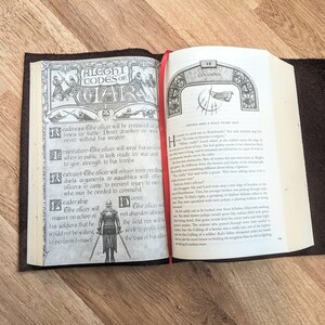 May include: An open book with a brown leather cover. The left page features a black and white illustration of a knight in armor with the text "ALEGHI CODES OF WAR" above the illustration. The right page features text from a book titled "COCOONS" with the text "Seven and a Half Years Ago" at the top of the page.