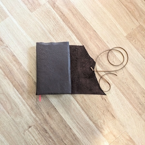 May include: A brown leather-bound journal with a matching brown leather strap and a brown leather tassel.