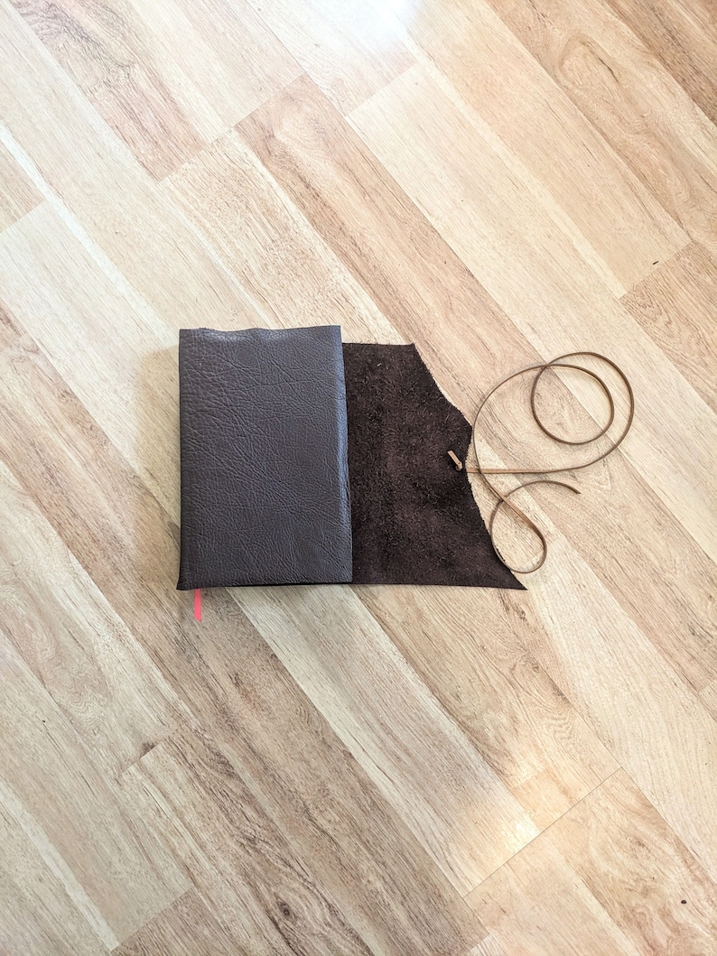 May include: A brown leather-bound journal with a matching brown leather strap and a brown leather tassel.