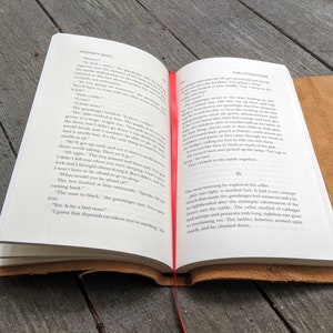 May include: Open book with a brown leather cover. The pages are open to a chapter titled "The Gunslinger" from the book "The Gunslinger" by Stephen King. The text on the page describes a scene where a gunslinger is talking to a boy.