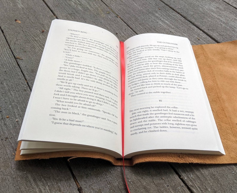 May include: Open book with a brown leather cover. The pages are open to a chapter titled "The Gunslinger" from the book "The Gunslinger" by Stephen King. The text on the page describes a scene where a gunslinger is talking to a boy.