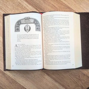 May include: Open book with a brown leather cover. The pages are open to a chapter titled "Decision". The text on the page discusses the importance of a decision and the consequences of making the wrong choice. The book is a fantasy novel with a medieval setting.