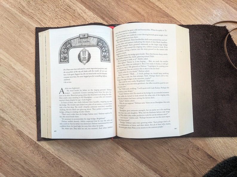 May include: Open book with a brown leather cover. The pages are open to a chapter titled "Decision". The text on the page discusses the importance of a decision and the consequences of making the wrong choice. The book is a fantasy novel with a medieval setting.