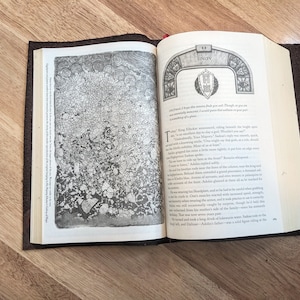 May include: An open book with a brown leather cover. The book is open to a page with a black and white illustration of a rock formation. The text on the page reads "Unity" and includes a quote about the importance of unity.