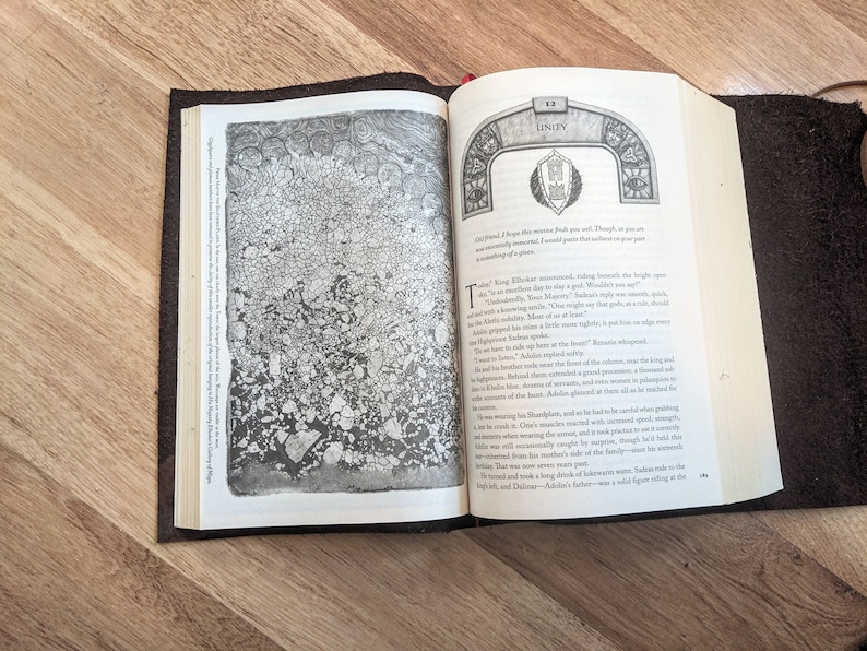 May include: An open book with a brown leather cover. The book is open to a page with a black and white illustration of a rock formation. The text on the page reads "Unity" and includes a quote about the importance of unity.