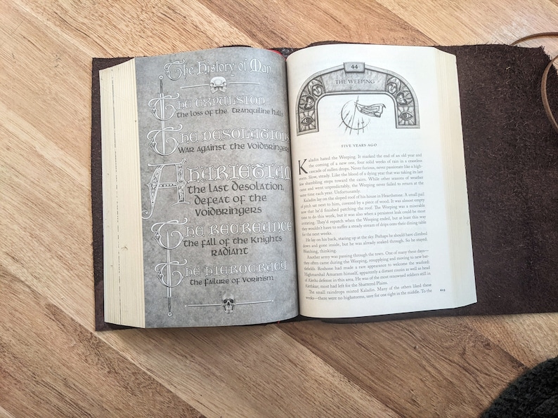 May include: A close-up of an open book with a brown leather cover. The pages are open to a section titled "The Weeping" and feature a detailed illustration of a skull and swords. The text on the page describes the "Last Desolation" and the "Fall of the Knights Radiant".