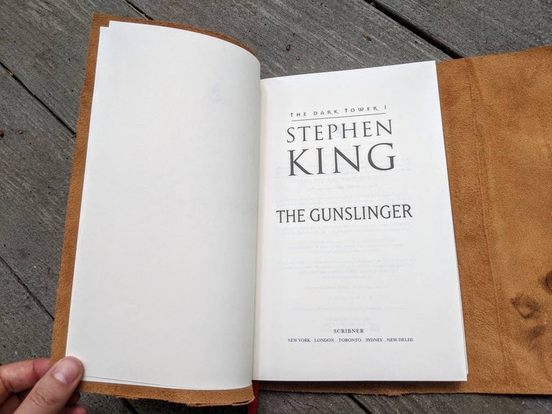 May include: A brown leather-bound book with the title "The Gunslinger" by Stephen King. The book is part of the "The Dark Tower" series.
