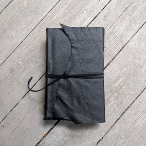 May include: A black leather-bound journal with a knotted leather strap closure.