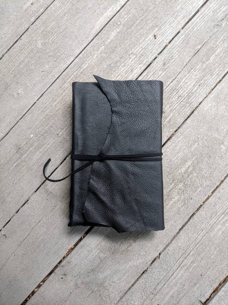 May include: A black leather-bound journal with a knotted leather strap closure.