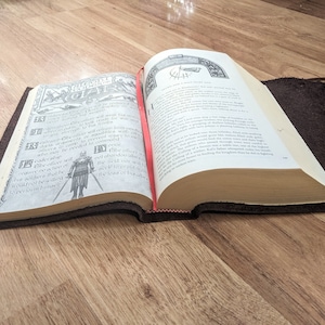 May include: An open book with a brown leather cover. The book is open to a page with a black and white illustration of a knight in armor. The text on the page is in English and reads "The Knight's Oath".