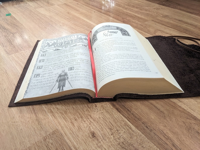 May include: An open book with a brown leather cover. The book is open to a page with a black and white illustration of a knight in armor. The text on the page is in English and reads "The Knight's Oath".