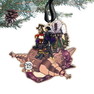 May include: Wooden Christmas ornament featuring a detailed illustration of several figures atop a stylized, brown, snail-like form. The ornament has a black ribbon for hanging and is decorated with a sun-like face and purple accents. The ornament is hanging from a pine branch.