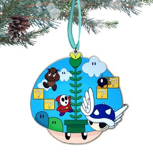 May include: A blue and white Christmas ornament featuring characters from the Super Mario Bros. video game. The ornament depicts a Koopa Troopa, a Goomba, a Boo, and a question block.
