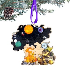 May include: Wooden Christmas ornament featuring a space-themed design with a sun, planets, and a cartoon character. The ornament is suspended by a purple ribbon. The background is a Christmas tree branch with a pine cone.