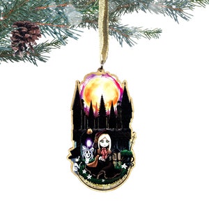May include: A wooden Christmas ornament featuring a silhouette of a castle with a full moon in the background. A girl with long blonde hair and a red dress is sitting in front of the castle with two other figures.