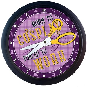 May include: A black clock with a purple and yellow patterned face. The clock face has the text "Born to Cosplay Forced to Work" and a pair of yellow scissors with a black handle.