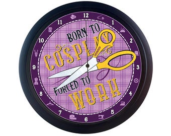 May include: A black clock with a purple and yellow patterned face. The clock face has the text "Born to Cosplay Forced to Work" and a pair of yellow scissors with a black handle.