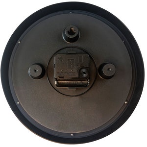 Pu&ograve; includere: Il retro di un orologio rotondo nero con una cornice nera. Il meccanismo dell'orologio &egrave; visibile, compreso il vano batteria e l'hardware di montaggio. L'orologio ha un design semplice e funzionale.