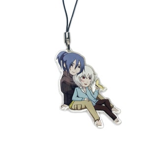 May include: Clear acrylic charm featuring an anime-style illustration of two characters. One character has blue hair and a dark jacket, the other has white hair and a blue sweater, holding a banana. The charm has a black lanyard.