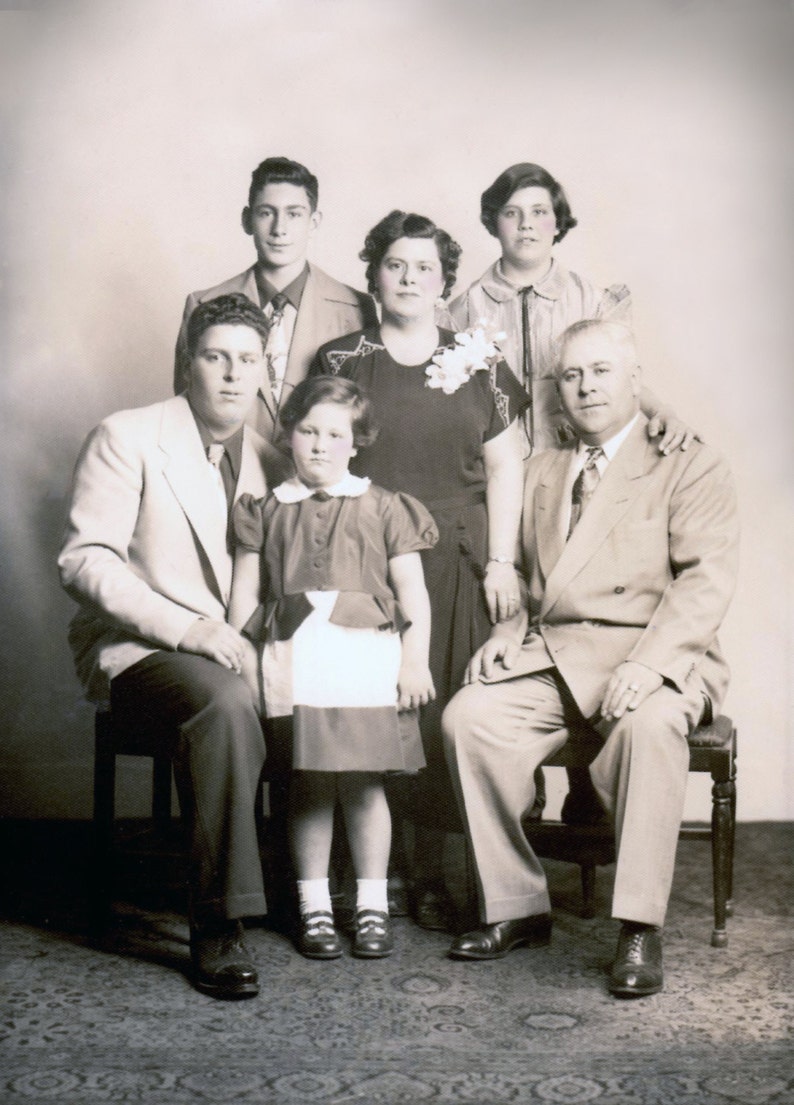 May include: A black and white photograph of a family of six. The family are standing in front of a plain background. The family are dressed in formal attire. The family are smiling.