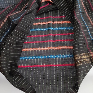 以下が含まれることがあります： ストライプ模様の黒い生地に、カラフルな刺繍のラインが施されています。生地は半分に折り畳まれており、内側の刺繍が見えています。