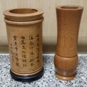 May include: Two wooden vases, one tall and slender, the other shorter and wider. The shorter vase has Chinese characters carved into the side.