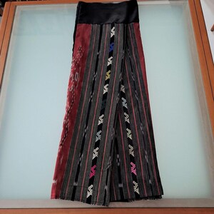 May include: A black and red wrap skirt with a black waistband and colourful geometric embroidery. The skirt is made of a woven fabric with a striped pattern.