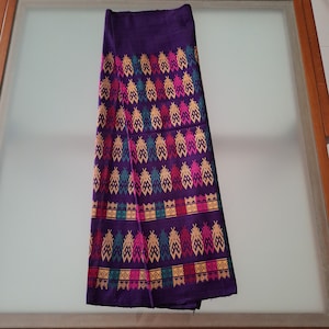 以下が含まれることがあります： 折りたたまれた濃い紫色の織物で、カラフルで様式化された葉の形が繰り返されています。デザインにはピンク、イエロー、グリーン、ターコイズの要素が組み込まれています。この生地は、おそらくシルクまたは同様の繊維である織物のように見えます。