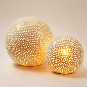 May include: Two spherical white ceramic lamps with a perforated surface pattern. Each globe features numerous small circular cutouts that allow warm light to glow from within, creating a textured, dotted appearance across the entire surface.