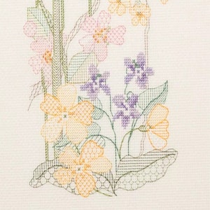 May include: A cross-stitch embroidery design featuring a variety of flowers in shades of pink, purple, yellow, and green. The flowers are arranged in a bouquet-like shape, with the stems and leaves intertwined.