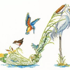 Puede incluir: Un ave garceta blanca se para sobre una pierna con la cabeza girada hacia un lado. El ave está posada sobre un zapato verde y frondoso con un ave martín pescador azul volando por encima. El zapato está rodeado de hojas verdes y flores.