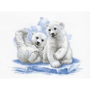 May include: A cross-stitch embroidery pattern featuring two white polar bear cubs sitting on a light blue ice floe. One cub is sitting upright while the other is lying on its back with one paw raised, all rendered in detailed white and blue thread.