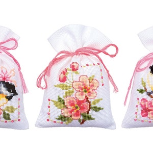 May include: Three white fabric sachets with pink ribbon ties. Each sachet features a cross-stitch design of a bird and pink flowers.
