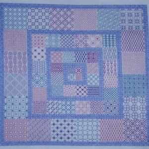 May include: A square, hand-stitched textile with a light blue border and a central design of nested squares. The squares are filled with various embroidered patterns in shades of blue, purple, and pink, creating a patchwork effect.