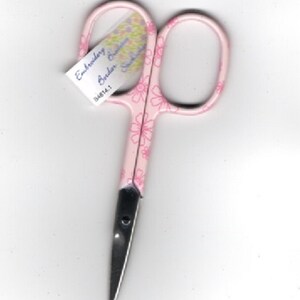 May include: Pink embroidery scissors with a floral design. The scissors have a silver blade and a label that reads "Embroidery Scissors Border Garden Scissors 34814.1".