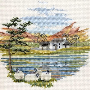May include: Cross-stitch embroidery depicting a rural scene with a white cottage, a lake, and sheep in a field. The sky is blue with white clouds, and the hills are green and brown.
