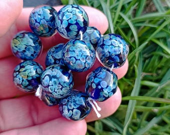 May include: A strand of blue glass beads with white speckles. The beads are round and have a textured surface. MuranoGlassAnastasia is written on the image.