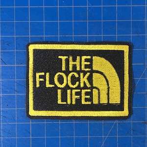 May include: Yellow embroidered patch with black background. The patch features a stylized mountain range and the text "THE FLOCK LIFE".