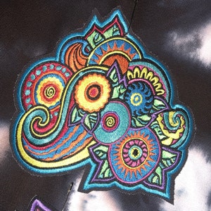 May include: A colorful embroidered patch with a paisley design featuring swirls, circles, and floral elements in shades of blue, green, yellow, orange, and pink.