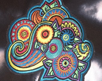 May include: A colorful embroidered patch with a paisley design featuring swirls, circles, and floral elements in shades of blue, green, yellow, orange, and pink.